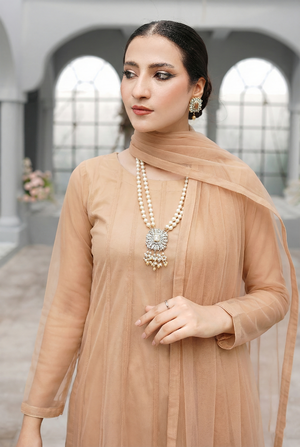 ROZAIB Champagne Peach luxury Bareeze net minimal kalidaar stitched suit. This premium ready to wear stitched dress features a 12-kali graceful flow fit, ultra-fine 0.3mm micro-mesh texture, and master-tailored vertical kali joints. A minimalist 3-piece stitched suit for women in a warm champagne-peach tone, paired with raw silk cigarette trousers and an airy Bareeze net dupatta. Designed for a traditional yet modern festive look with zero embroidery.